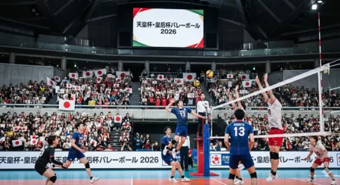 2026年天皇杯・皇后杯全日本バレーボール選手権大会の試合会場の様子。ネット際での迫力あるスパイクシーンと、日本国旗を掲げて応援する満員の観客席。
