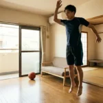 自宅のリビングでジャンプ力を鍛えるバスケットボールの室内トレーニング風景。垂直跳びをする男性と床に置かれたボール。