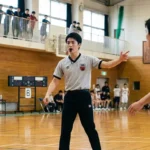 バスケットボールの試合でホイッスルを吹きジェスチャーを送るJBA公認審判員。審判ライセンスの取得方法や種類の解説。