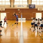 体育館で6人制バレーボール（左側）と9人制バレーボール（右側）のチームが対峙する比較画像。左側の6人制は攻撃的なスパイクシーン、右側の9人制は大人数での守備陣形を描いており、コート内の人数差やルールの違いを視覚的に解説している。背景には「6人制」「9人制」のパネルとバレー部の横断幕。