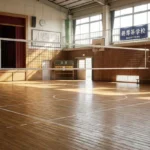 日本の学校の体育館に設置されたバレーボールコートとネット、窓から日差しが差し込む木製の床と部活動の風景