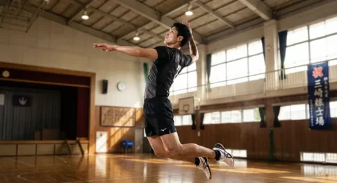 体育館で高くジャンプし、スパイクのフォームを整えるバレーボール選手の空中姿勢。打点を高くするための腕の引き方とジャンプのタイミング。