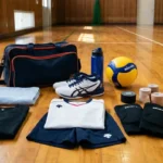 バレーボール初心者の練習に必要な道具一式。体育館の床にシューズ、ウェア、サポーター、ボール、テーピング、スポーツバッグが並んでいる様子