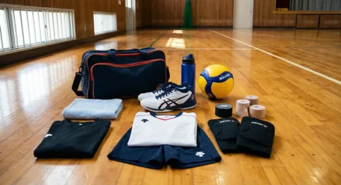 バレーボール初心者の練習に必要な道具一式。体育館の床にシューズ、ウェア、サポーター、ボール、テーピング、スポーツバッグが並んでいる様子